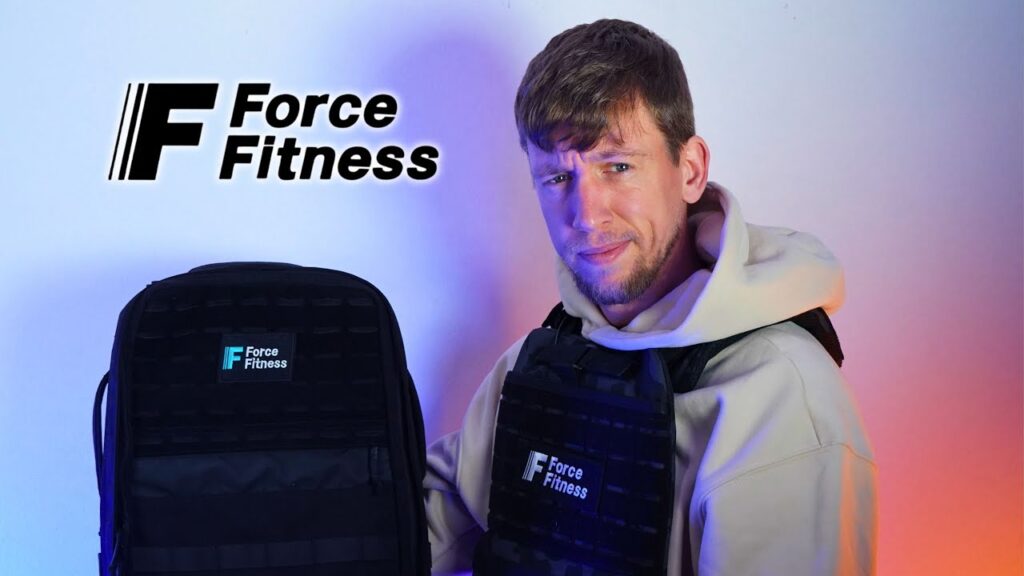 Man in white hoody holding up a force fitness backpack while also wearing a force fitness weighted vest and looking questioningly at the camera.