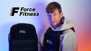 Man in white hoody holding up a force fitness backpack while also wearing a force fitness weighted vest and looking questioningly at the camera.
