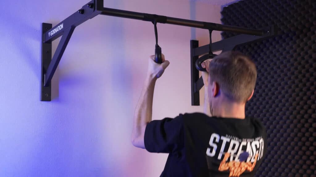 Man in black shirt doing rotating grip pull-ups using the kensui 360 grips attached to a gornation wall pull-up bar by rotator straps.