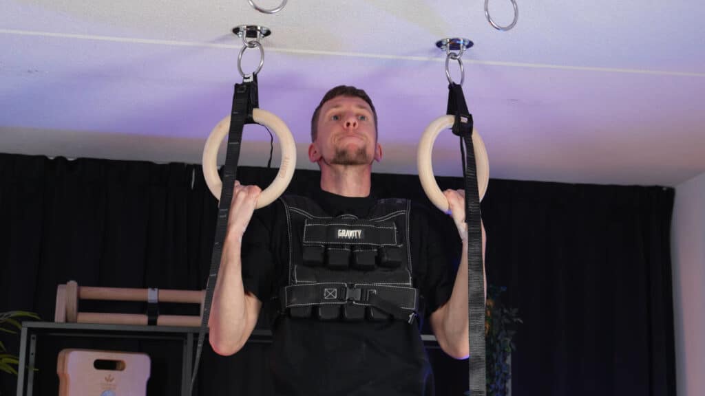 Man doing chin ups on the gravity fitness gymnastic rings while wearing a gravity fitness weighted vest.
