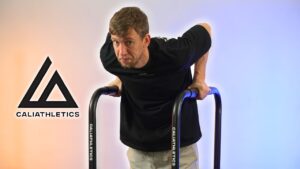 Man in black shirt doing dips on the Caliathletics Adjustable Dip Bars and looking questioningly at the viewer.