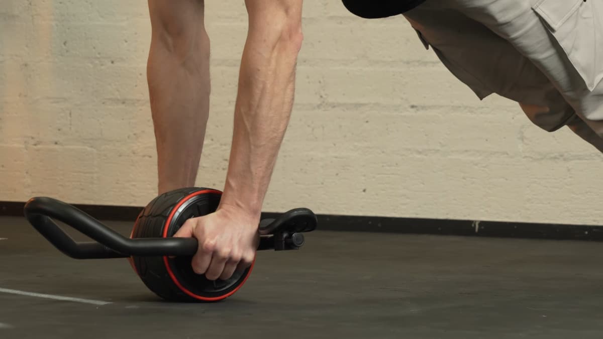 Man holding the handles of the dmoose ab roller close to the wheel in an attempt to get a neutral grip unassisted ab rollout.