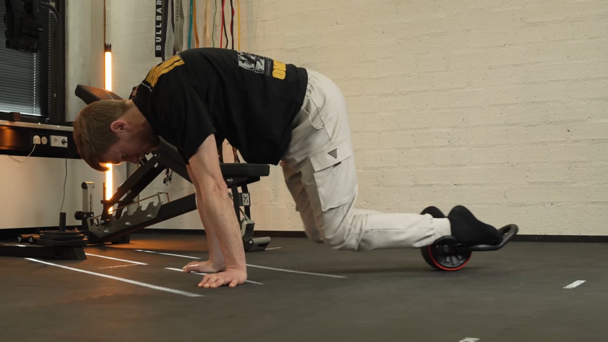 Man in black shirt doing mountain climbers on the dmoose ab roller in a gym setting.