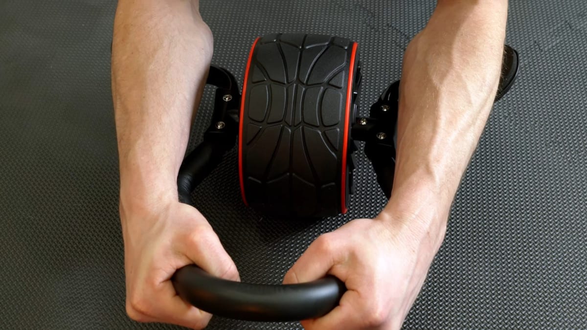 A man's hands holding the braces of the dmoose ab roller and the elbows resting on the rests on either side of the wheel.