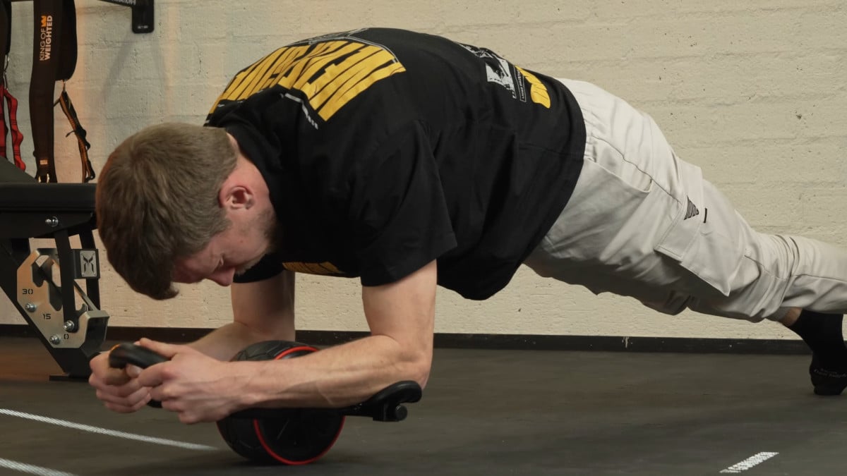 Man in the midst of doing an assisted ab rollout on the dmoose ab roller in a gym setting.