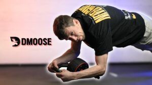 Man in black shirt doing assisted ab rollouts on the DMoose Ab Roller and looking questioningly as the camera.