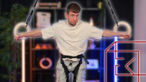 Man strapped into the FitnessKit Lift Dream Machine and holding two gymnastic rings while looking questioningly at the viewer.