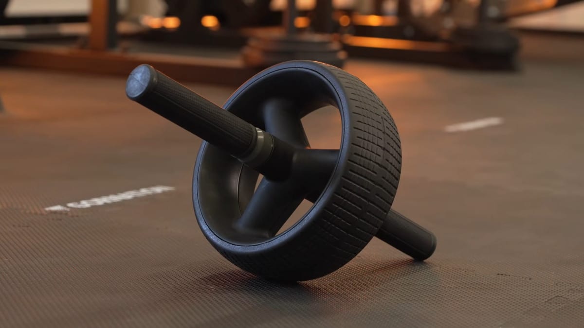A rogue ab wheel resting on one handles by itself on the floor of a gym.