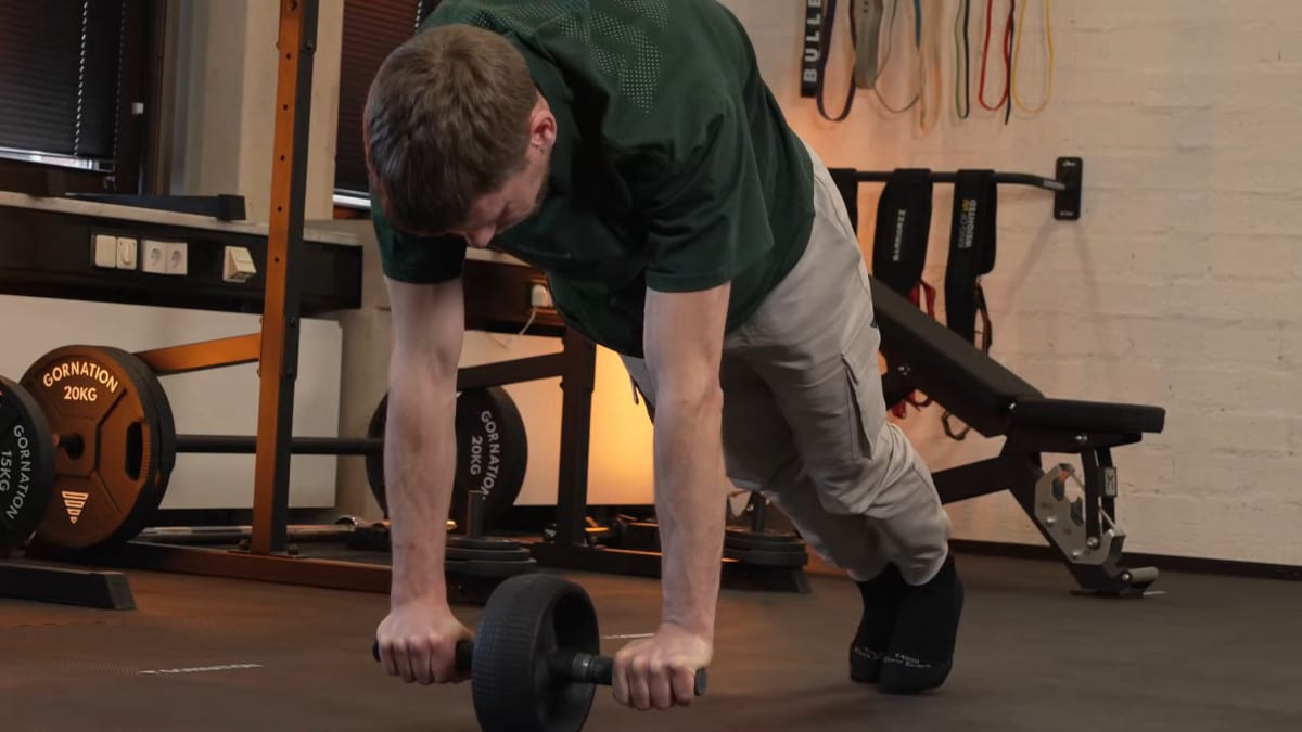 Man in green shirt in the middle of a proper ab roll out on the rogue ab wheel with only his toes touching the floor and his legs straight.