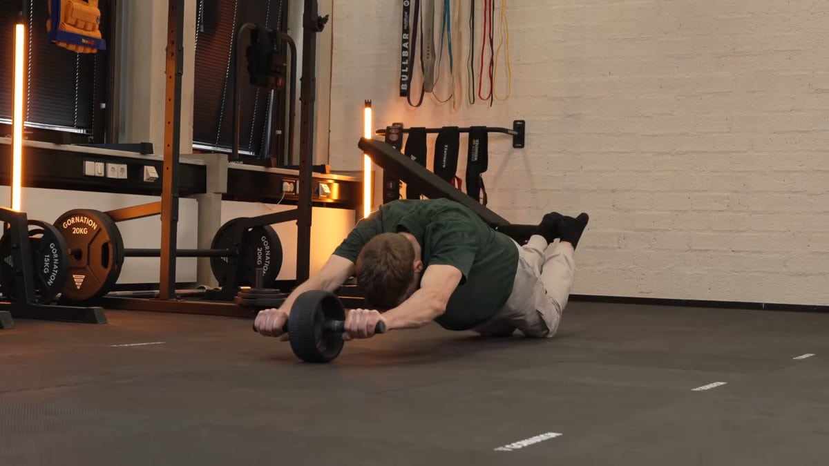Man in green shirt doing ab roll outs on the rogue ab wheel in a gym setting.