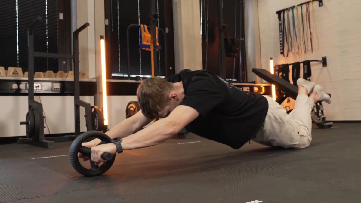 Man in black shirt doing ab roll outs on the rogue ab wheel while resting on his knees for support.