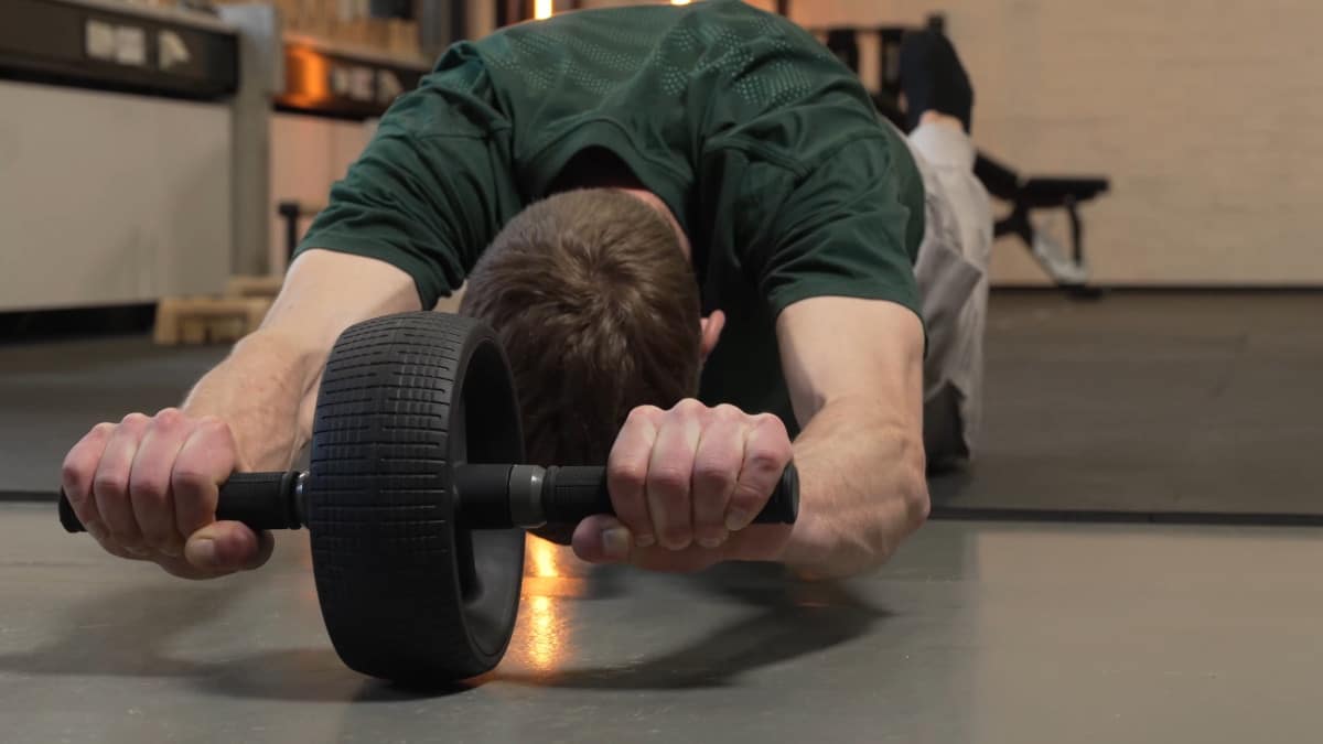 Man in green shirt doing ab roll outs on the rogue ab wheel, resting on his knees.