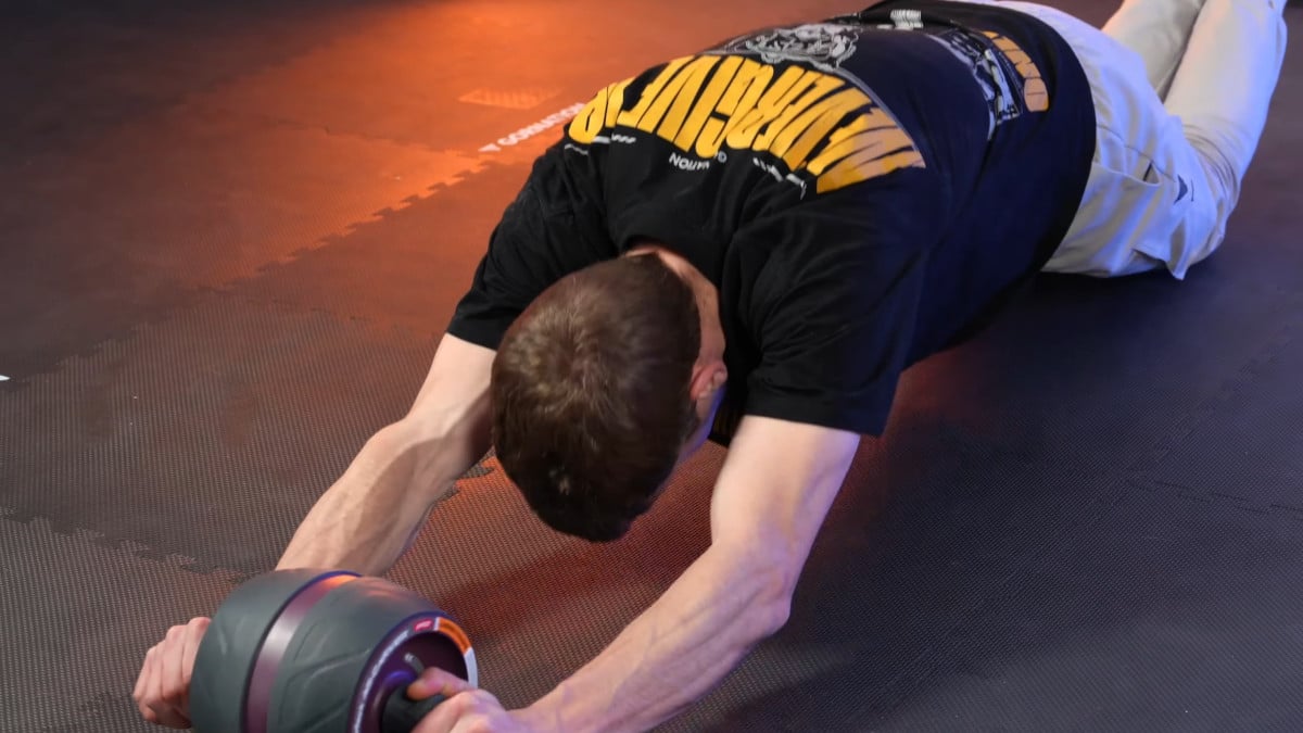 Man doing an ab rollout on his knees with the Perfect Fitness Ab Carver Pro, his arms showing clear signs of muscle tension.