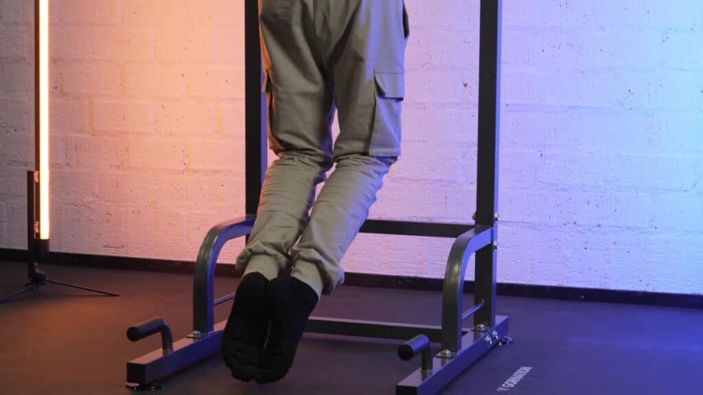 Man in green trousers doing pull-ups on the relife power tower, bending his knees to avoid stepping on the floor during the exercise.