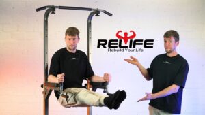 Man appearing twice in the image, once doing an L-sit on the relife power tower and the second where is standing with arms in a presenting fashion towards the same power tower.