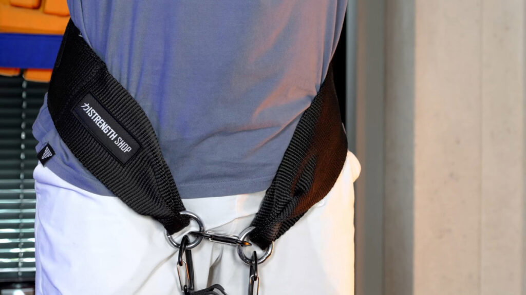 Man in blue shirt wearing a strength shop dip belt with all three carabiners attached and ready to do an exercise.