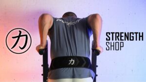 Man in blue shirt and turned away from the camera, doing dips on a dip bar while wearing the Strength Shop Dip Belt.