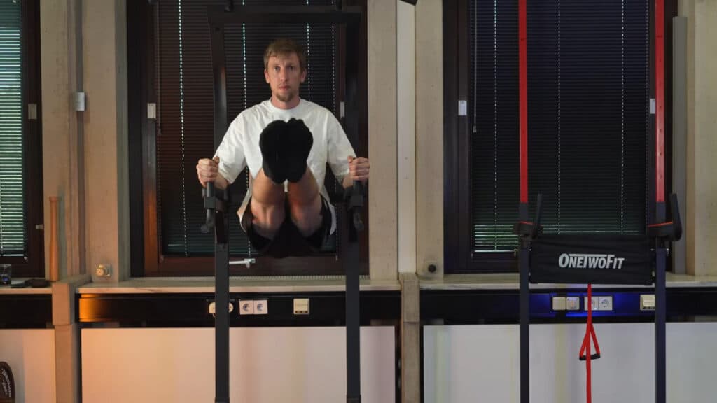 Man in white shirt doing leg raises on a decathlon power tower.