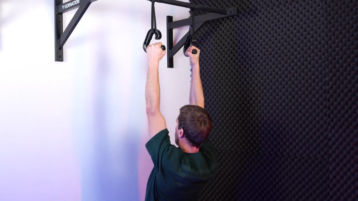 Man doing pull-ups on the kensui swissies attached to rotator bands, showing how low he hangs near to the floor.