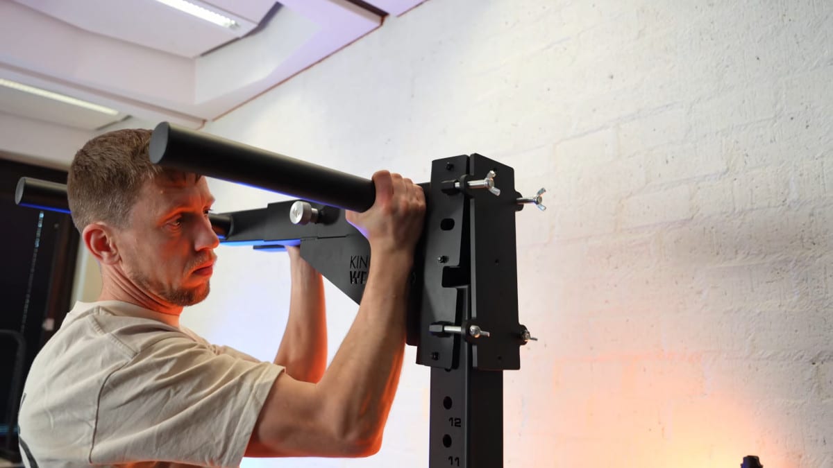 Man looking intently as he places the dip bars of the king of weighted adjustable dip station in place, prior to fastening them with wingnuts and a safety pin.