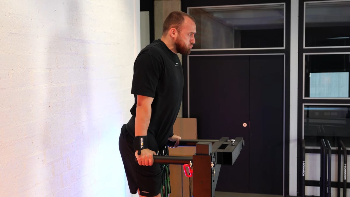 Man in black shirt doing weighted dips on the king of weighted adjustable dip station, and physically exerting himself in doing so.