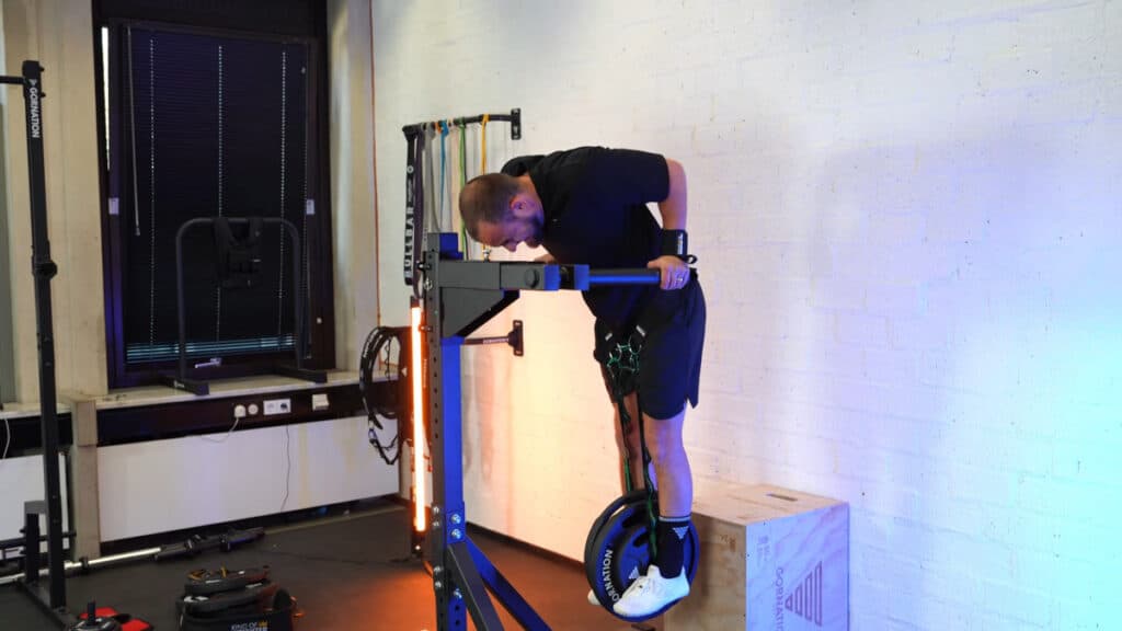 Man in black shirt doing weighted dips on the king of weighted adjustable dip station and being physically strained in his exercise.