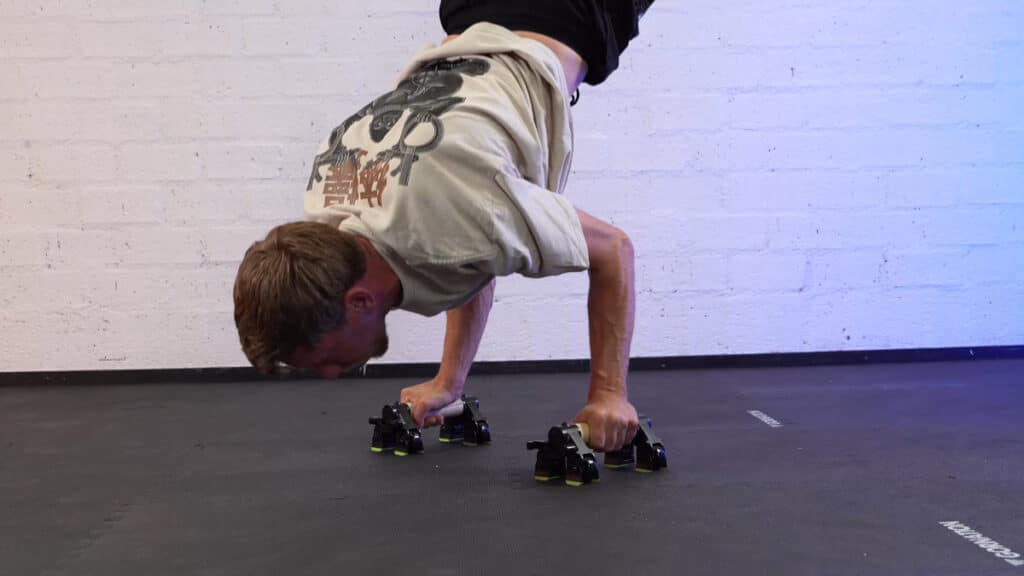 Man in white shirt doing handstand push ups on the duonamic axis in parallette mode.