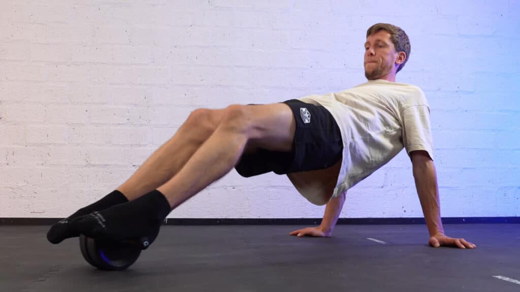 Man in white shirt doing core exercises on a vinsguir ab roller on a gym floor.