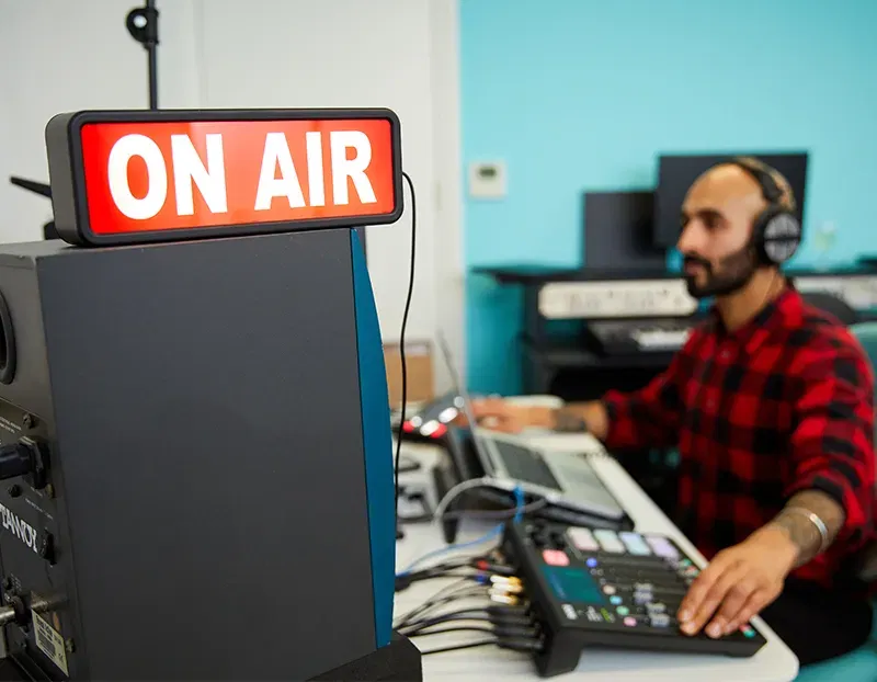 A man broadcasting using a laptop with an 'On Air' sign in the foreground