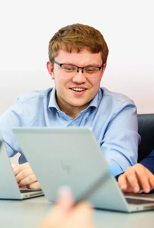 A smiling man in glasses looks at a colleague's laptop
