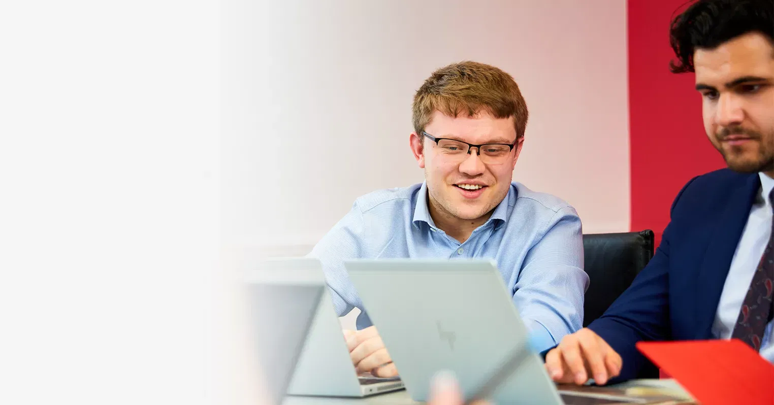 Two men sit side by side, looking at laptop screens