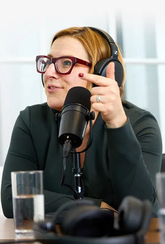 A photo of a woman wearing headphones and talking into a podcast microphone