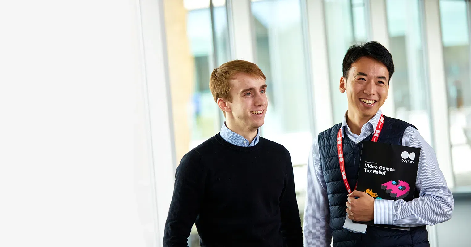 Photo of two smiling men, the one on the right is weating a lanyard and holding a copy of an Oury Clark guide to video games tax relief