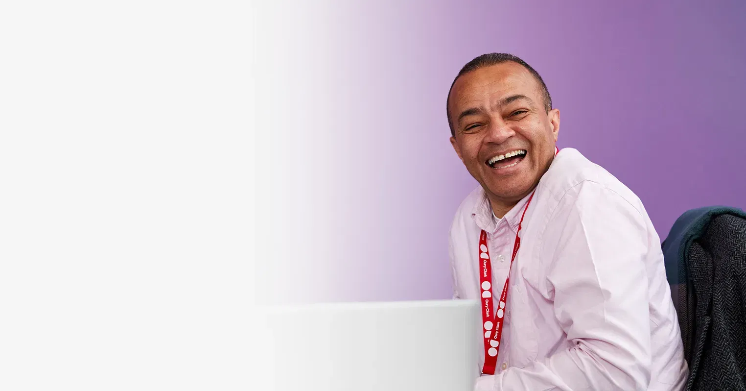 An image of a laughing man in pink shirt wearing an Oury Clark lanyard