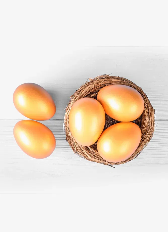 A small nest seen from above, with three golden eggs inside it, and two more outside
