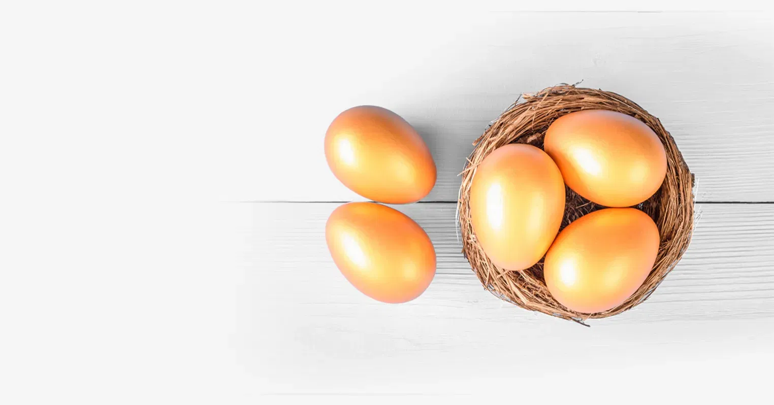 A small nest seen from above, with three golden eggs inside it, and two more outside