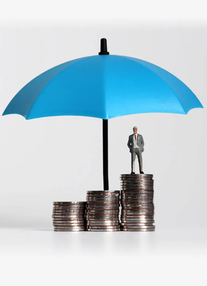 Three different sized stacks of coins, with a toy figure of a man stood on the tallest, with a blue umbrella sheltering them all