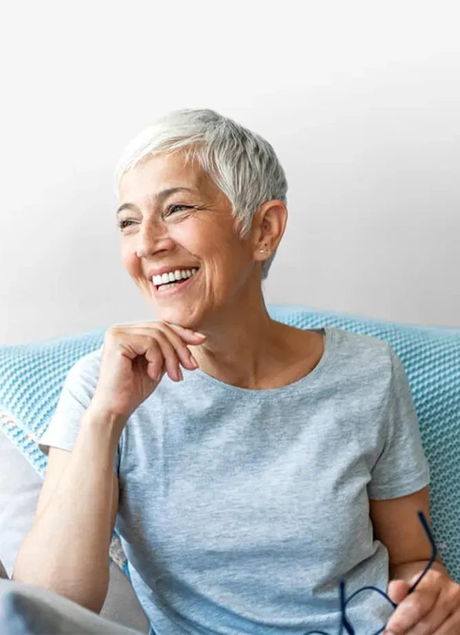 A woman sitting on a chair, she's holding her glasses in her hand and laughing