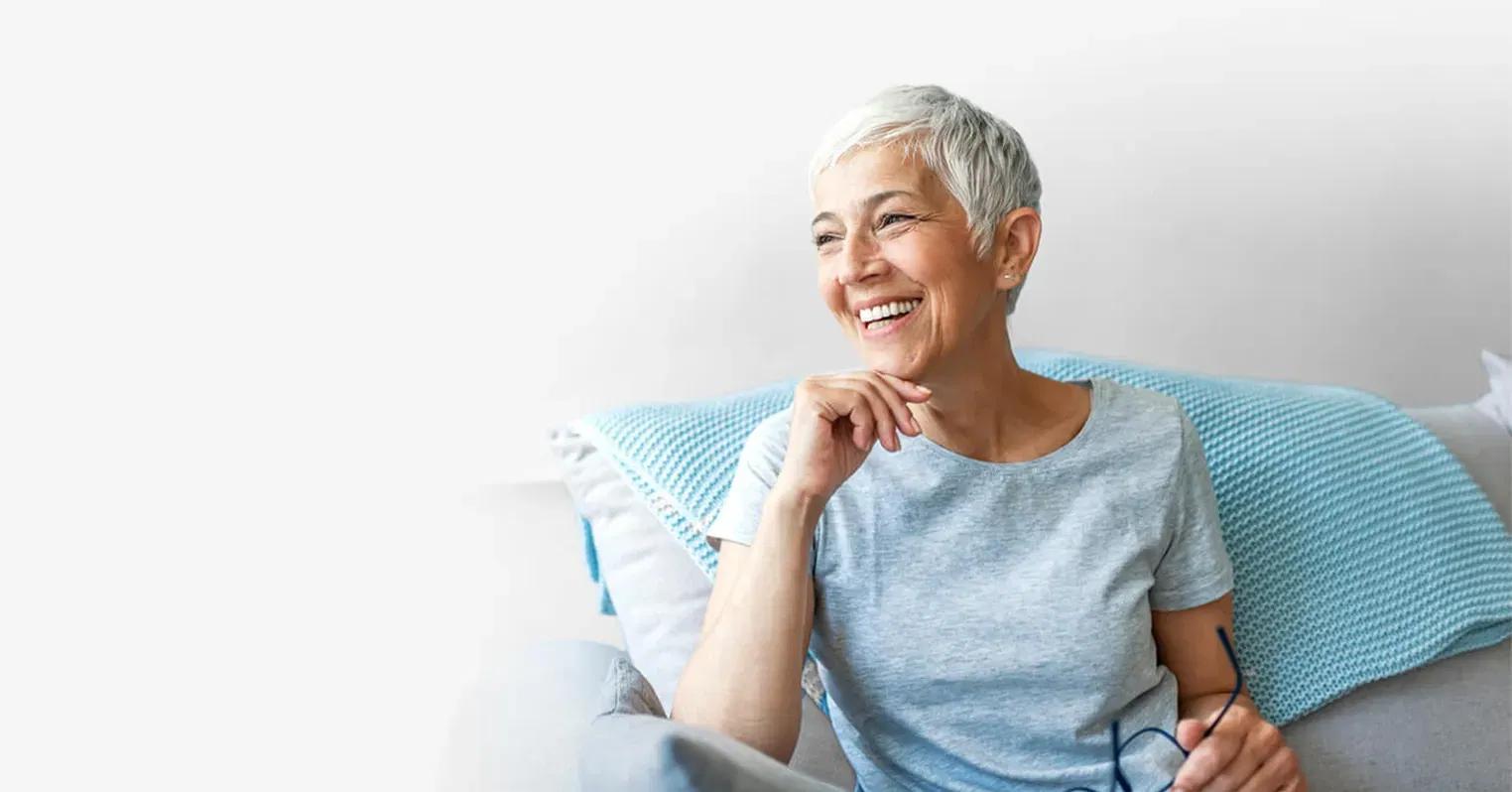 A woman sitting on a chair, she's holding her glasses in her hand and laughing