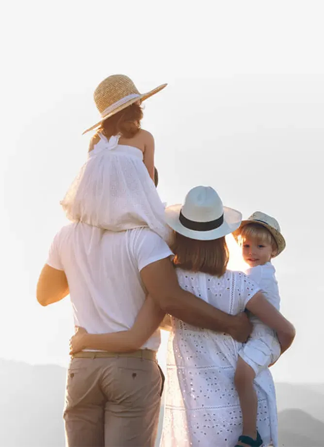 Image of a family of four - a man, a woman and a boy and girl child. The children and the mum are wearing hats, the boy child looking back towards the camera