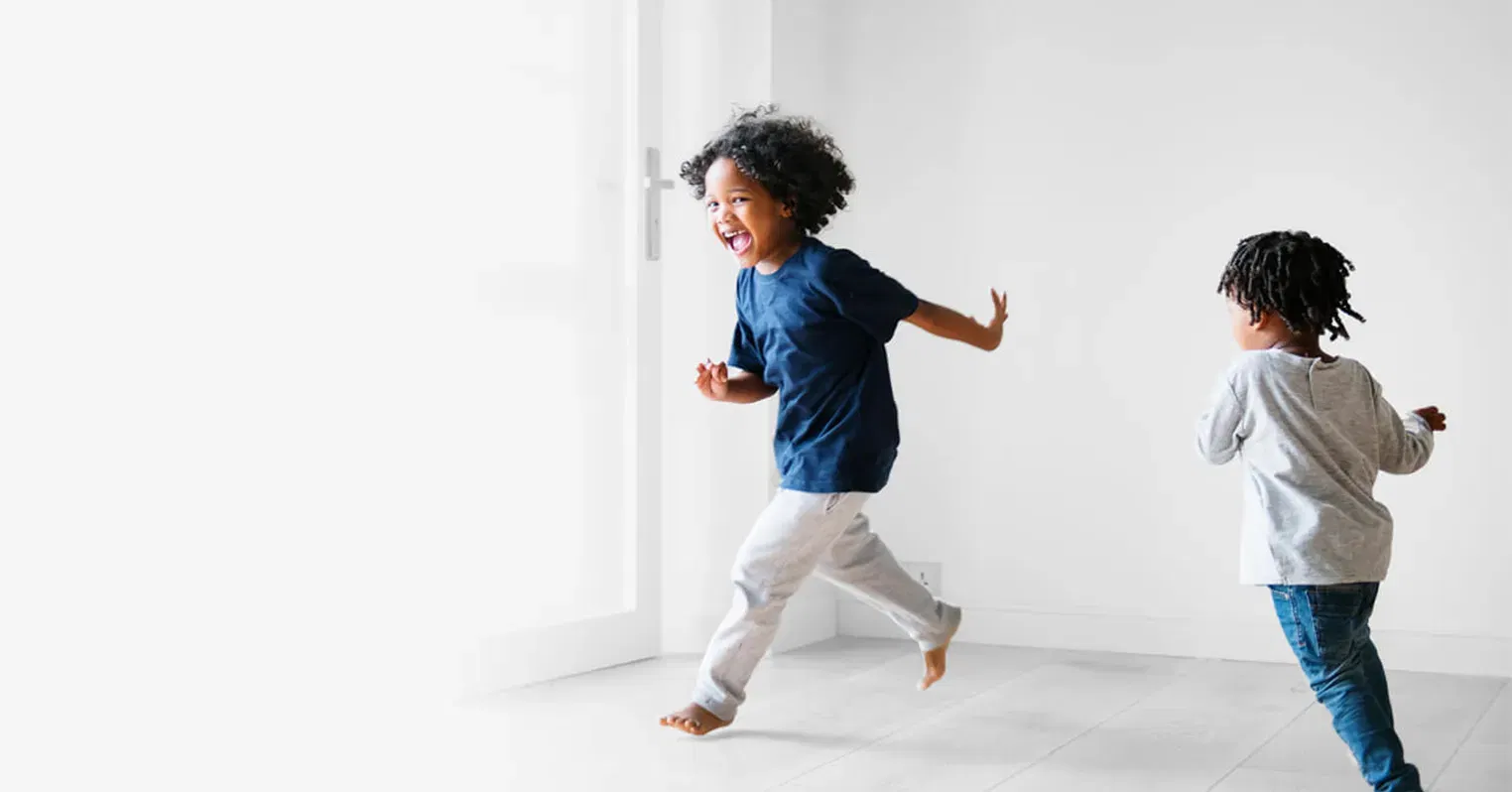 Photo of two young children chasing around an empty room and laughing