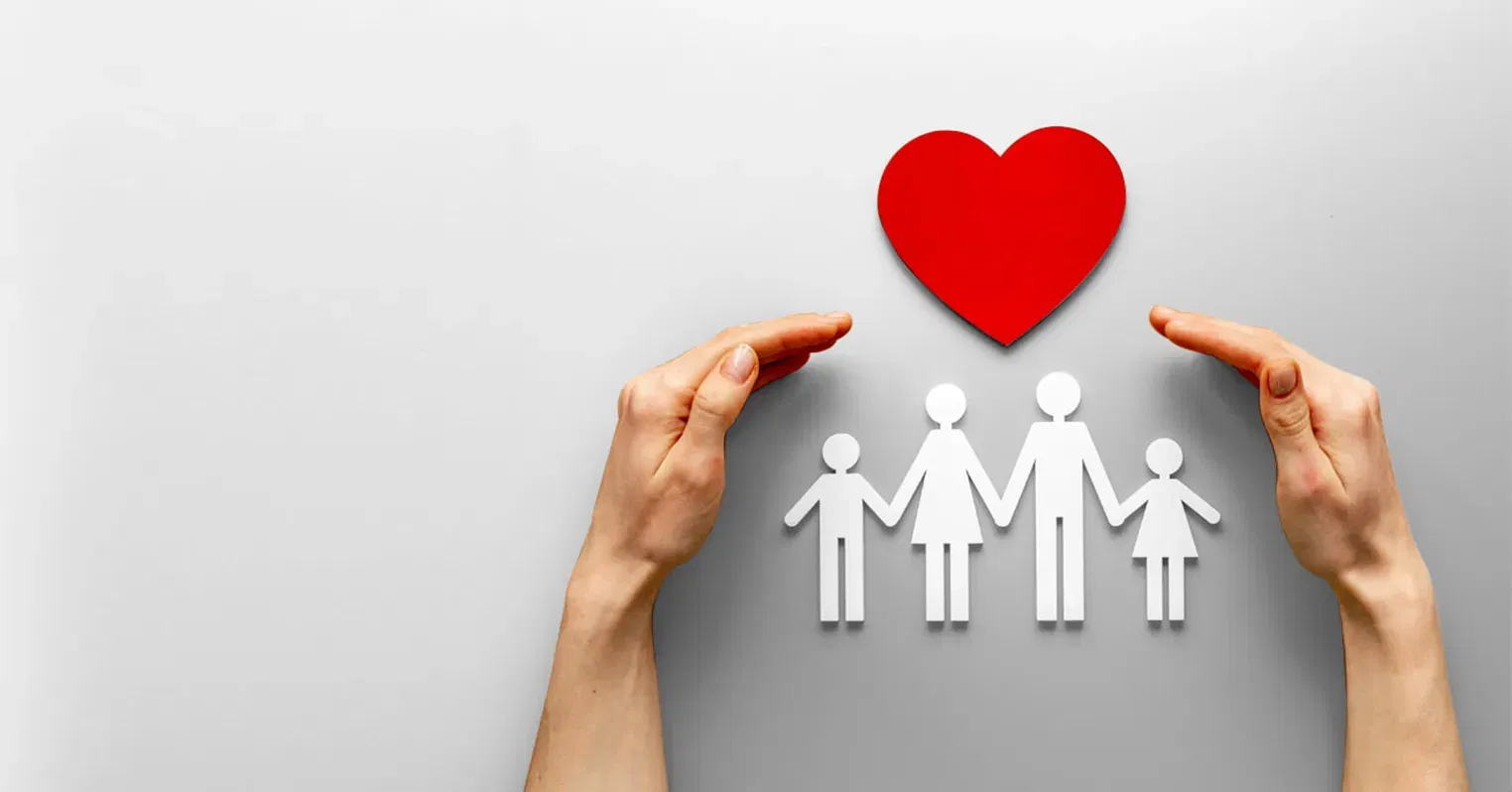 Cut out figures of a two parent, two child family, with a red heart above them and a pair of human hands curling around as if to protect them