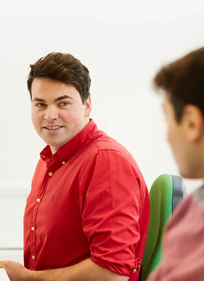 A man in a red shirt looks at an out of focus man in a pink jumper