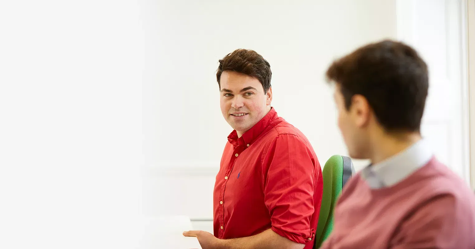 A man in a red shirt looks at an out of focus man in a pink jumper
