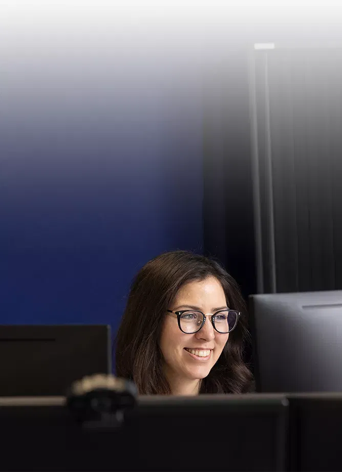 Dark-haired woman with glasses smiling while looking at computer monitor